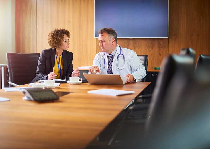 healthcare administrator talking with physician at board meeting table