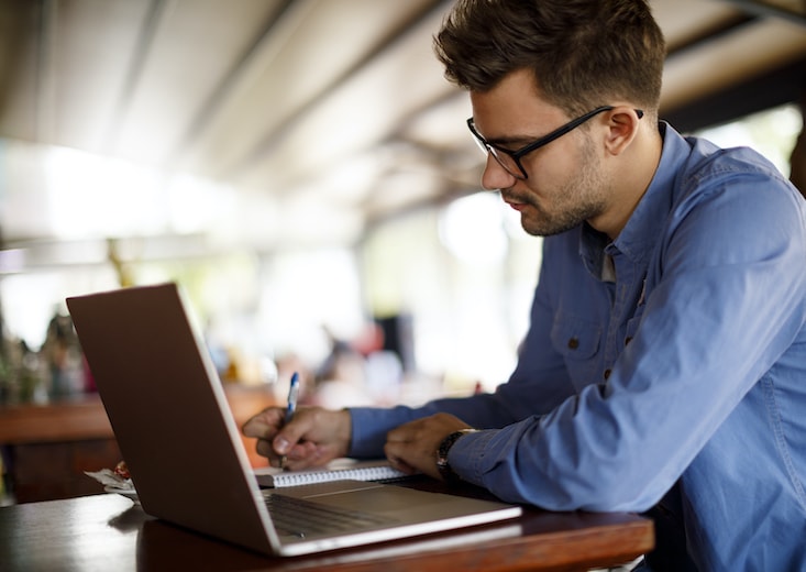 male student taking notes in tablet beside laptop